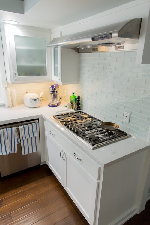 Modern kitchen with white cabinets, gas stove, stainless hood, mixer, rice cooker, and striped towels on dishwasher.